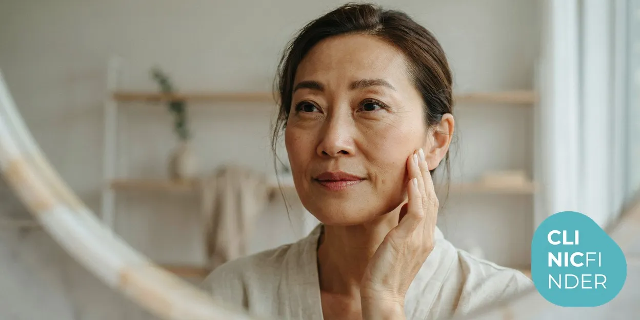 A woman in her early fifties with radiant, well-hydrated skin gently touching her cheek in soft natural daylight, reflecting Profhilo’s focus on skin quality